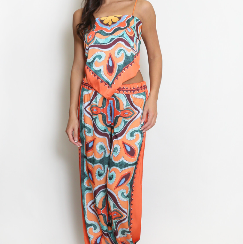 A woman modeling a sleeveless, wide-leg jumpsuit with a vibrant orange, teal, and red paisley pattern against a plain white background.