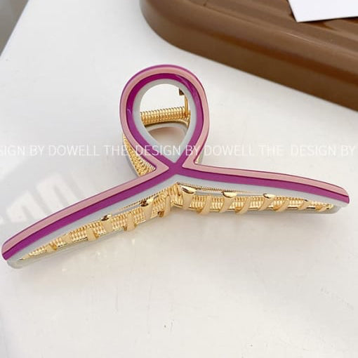Pink and gold hair clip on a white surface with a brown tray in the background.